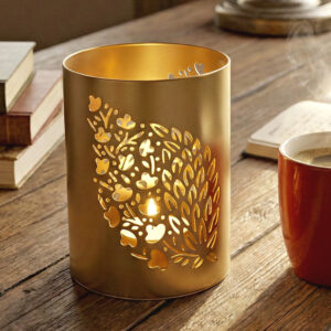 Champagne gold metal tealight holder Laser cut iron candle stand for home Modern minimalist desk decor accessories Diwali decoration items for living room Shadow casting votive candle holder Gold cylinder candle holder table centerpiece Cozy aesthetic room decor for study Premium metal home decor manufacturer Unique housewarming gifts under 500 Luxury nature inspired candle jar